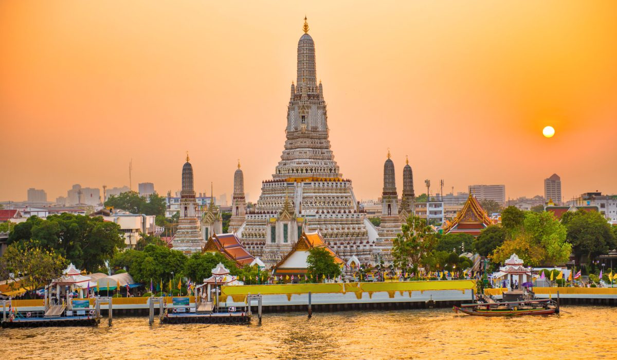 Beautiful Temple of Dawn or Wat Arun and Thonburi west bank of Chao Phraya River at sunset with shining sun. Bangkok, Thailand